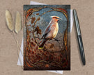Greeting card with a bird design on a textured surface with a pen and dried plants.