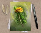 Greeting card with a dandelion design on a textured surface with a pen and dried plants.