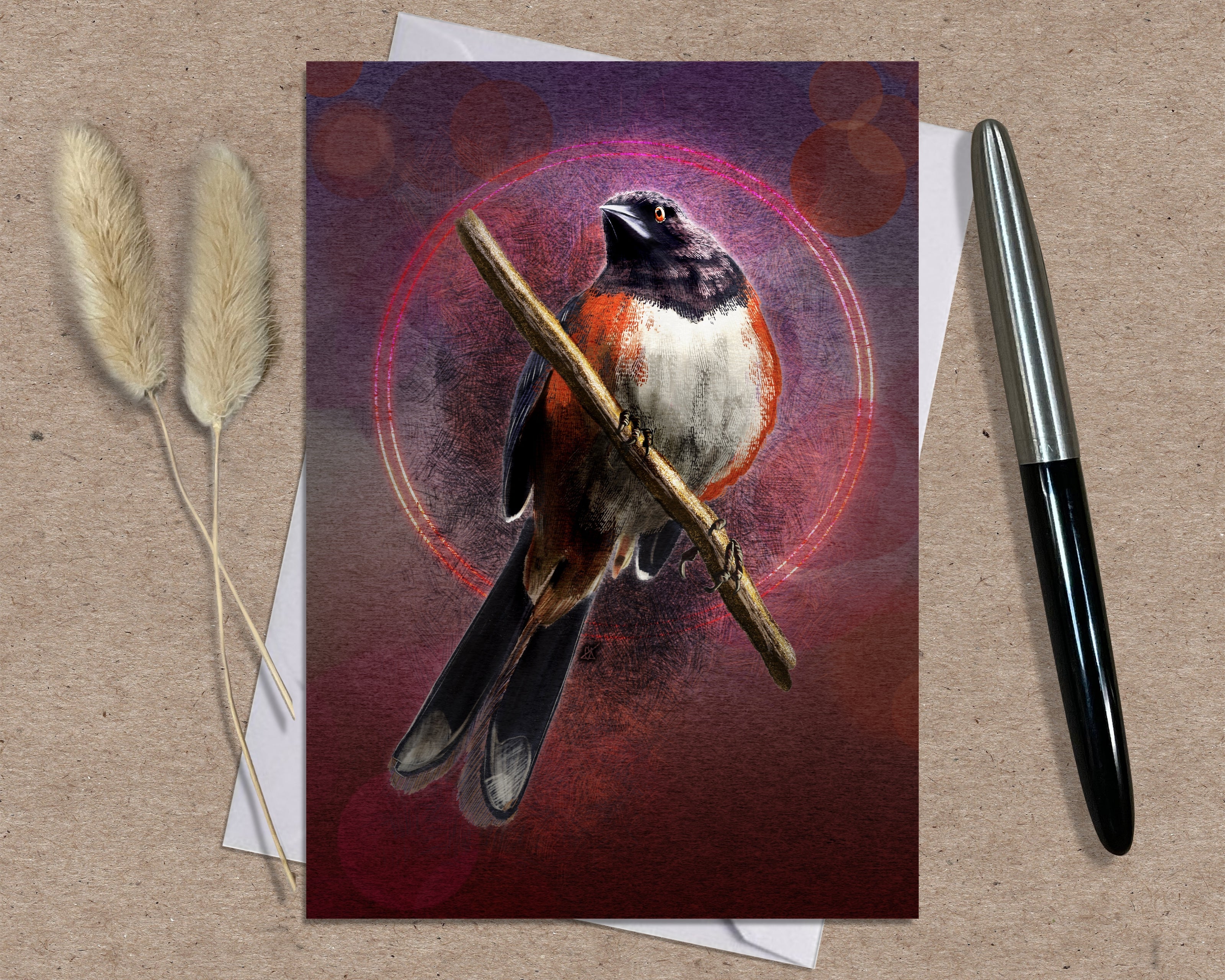Greeting card with a bird illustration on a textured surface with a pen and dried plants.