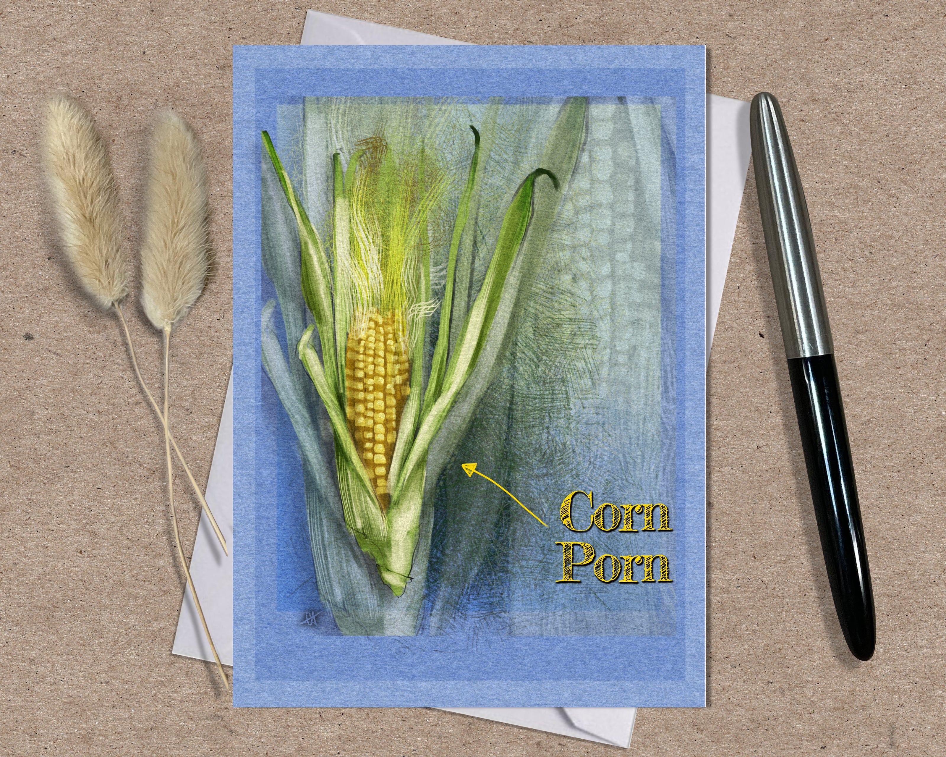Card with illustration of corn and text 'Corn Porn' on a textured surface with a pen and dried plants.